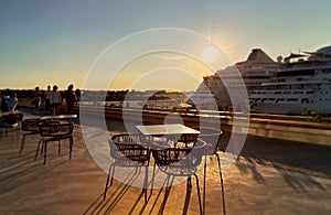 Sunset at pier in harbor cafe table and chair on fron background big cruise ship and people relaxing Tallinn new port Baltic sea