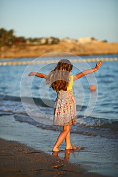 Sunset portrait of a happy dancing caucasian girl  in summer dress at the seashore