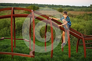 Sunset portrait of  thoughtful caucasian boy climbing at the outdoor modern playground