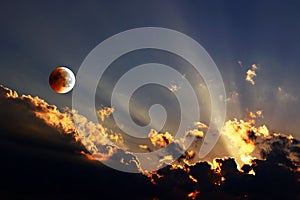 Sunset with rays of light and rising moon with lunar eclipse in the evening sky