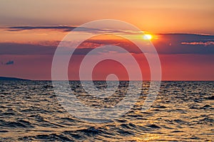 Sunset red sun in clouds over sea with waves on water, dark clouds