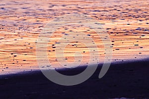 sunset reflected in the water with pebbles and sand on the beach