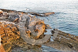 Sunset rocky beach with ladder for swimming in Istria, Croatia.