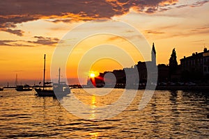 Sunset in Rovinj, Croatia, with a boat sailing in the Adriatic Sea and the sunrays reflected on the water, with the old town at