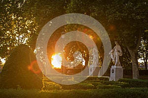 Sunset by Royal Palace or Palacio Real with Plaza de Oriente park statues and sun flares through the trees, Madrid Spain