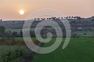 Sunset with sand suspended in the atmosphere, coluring the sky red, over some green fields and hills photo