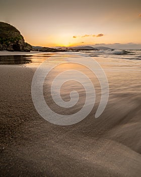 Sunset on a sandy beach with waves in long exposure