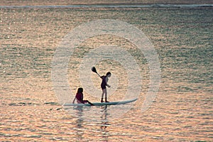 Sunset scene on  background. Two little girls silhouettes  are padddling