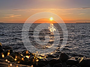 Sunset at sea on beach seastone sun beam loght reflection on water wave nature background.