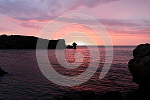 Sunset on the sea, rocks and sun, silhouette and boat with fishermen.