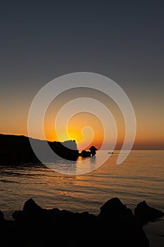 Sunset on the sea, rocks and sun, silhouette and boat with fishermen.