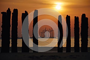 Sunset seascape with a selective focus of a wind farm, visible through silhouettes of wooden poles