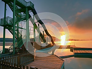 Sunset shore and toboggan slides at lake,. High ladder tower with sliding track.