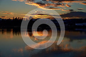 Sunset showing golden clouds and tree silhouettes reflected in the dark blue river estuary waters.