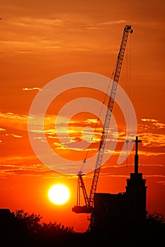 Sunset silhouette construction building tower crane cross on the roof of the church of the Sloane