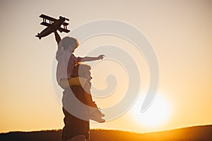 Sunset silhouette of Happy father and child son with airplane dreams of traveling. Father carrying his son on shoulders.