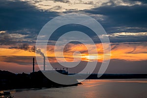 Sunset silhouette of industrial plant with a smoking pipe located on a river