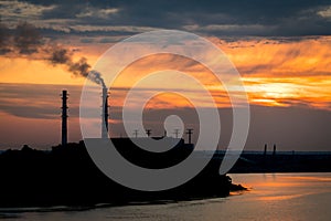 Sunset silhouette of industrial plant with a smoking pipe located on a river
