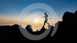 Sunset silhouette of skyrunner man descending from alpine ridge with poles