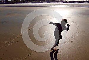 Sunset silhouette of a young boy running on beach sand