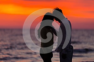 Sunset silhouette of young couple in love hugging at beach