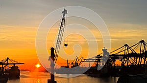 Sunset silhouettes cargo ships, cranes at sea port. Industrial loads freight at dock. Trade, transport infrastructure