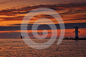 Sunset with silhouettes of tourists at the windmill shaped lighthouse on the Baltic Sea in SwinemÃ¼nde. Swinoujscie, Poland