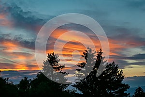 Petzen - Sunset sky with clouds in the background and silhouette of trees in the foreground. The sky has vibrant orange pink color photo