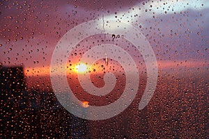 Sunset sky with clouds of the sea and house background seen through raindrops on glass.