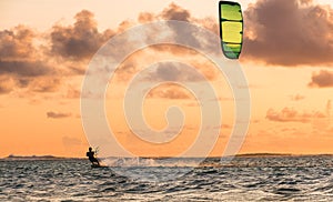 Sunset sky over the Indian Ocean bay with a kiteboarder riding kiteboard with a green bright power kite. Active sport people and