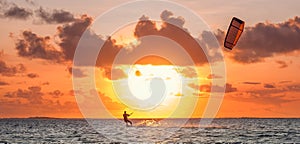 Sunset sky over the Indian Ocean bay with a kiteboarder riding kiteboard with a green bright power kite. Active sport people and