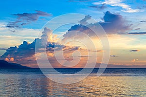 Sunset sky and sea. Seaside sunset with orange and blue clouds. Tropical sea and distant island silhouette.