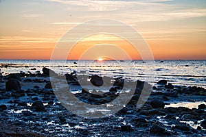 Sunset, stone beach with small and large rocks in front of the illuminated sea