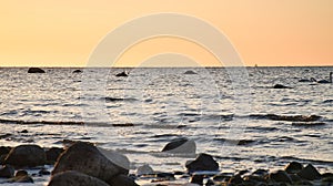 Sunset, stone beach with small and large rocks in front of the illuminated sea