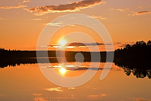 Sunset with strong colors. Lake, horizon, orange sky with cloudlets, glowing sun and reflection.