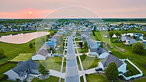 Sunset suburban neighborhood with pond one-story and two-story houses green lawns visible sun aerial