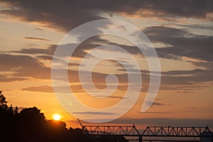 Sunset on a summer evening on the illuminated sky in pink and purple colors over the river against the background of the railway