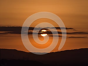 Sunset with sun shining through dark clouds above hills on horizon with orange colored sky viewed from Koblenz, Germany.