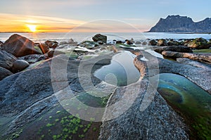 Sunset with sunburst and red golden tones in the horizon at Uttakleiv beach with the famous dragons eye infront.