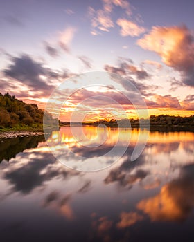 A sunset or sunrise scene over a lake or river with dramatic cloudy skies reflecting in the water on a summer evening or morning