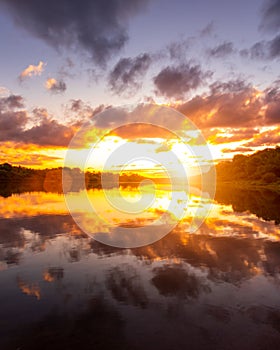 A sunset or sunrise scene over a lake or river with dramatic cloudy skies reflecting in the water on a summer evening or morning