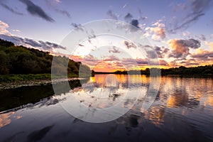 A sunset or sunrise scene over a lake or river with dramatic cloudy skies reflecting in the water on a summer evening or morning