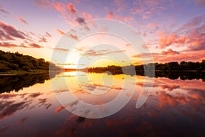 A sunset or sunrise scene over a lake or river with dramatic cloudy skies reflecting in the water on a summer evening or morning