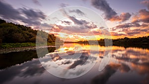 A sunset or sunrise scene over a lake or river with dramatic cloudy skies reflecting in the water on a summer evening or morning