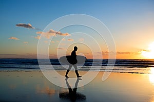 Sunset surfing. Silhouette of man surfer walking with a surf board in his hands across the ocean shore.