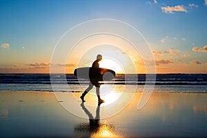 Sunset surfing. Silhouette of man surfer walking with a surf board in his hands across the ocean shore.