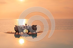 Sunset at table dinner over infinity swimming pool with seascape and horizon, romance