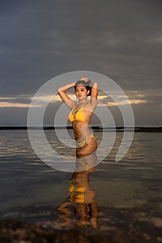 Sunset time on the beach. Attactive Asian woman posing in yellow bikini. Tanned skin. Slim fit body. Water reflaction. Tropical