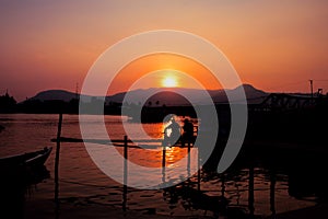 Sunset time on river. Orange sunset landscape with pier and men. Vivid orange sky view.