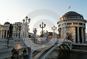 Sunset time with Sculptures in art bridge at Skopje, capital of North Macedonia. Vintage lamps in the street and big building with